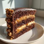 Close-up of a rich slice of chocolate caramel toffee crunch cake showing three dark layers and caramel filling.