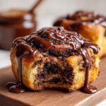 Close-up of a soft chocolate cinnamon roll with a bite taken out, drizzled heavily with chocolate glaze.