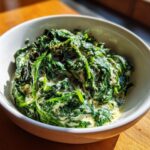 A close-up of vibrant green spinach coated in a rich, creamy sauce in a white bowl, showcasing the creamed spinach recipe.