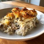 A generous serving of creamy chicken wild rice casserole with a golden, crispy topping in a white bowl.