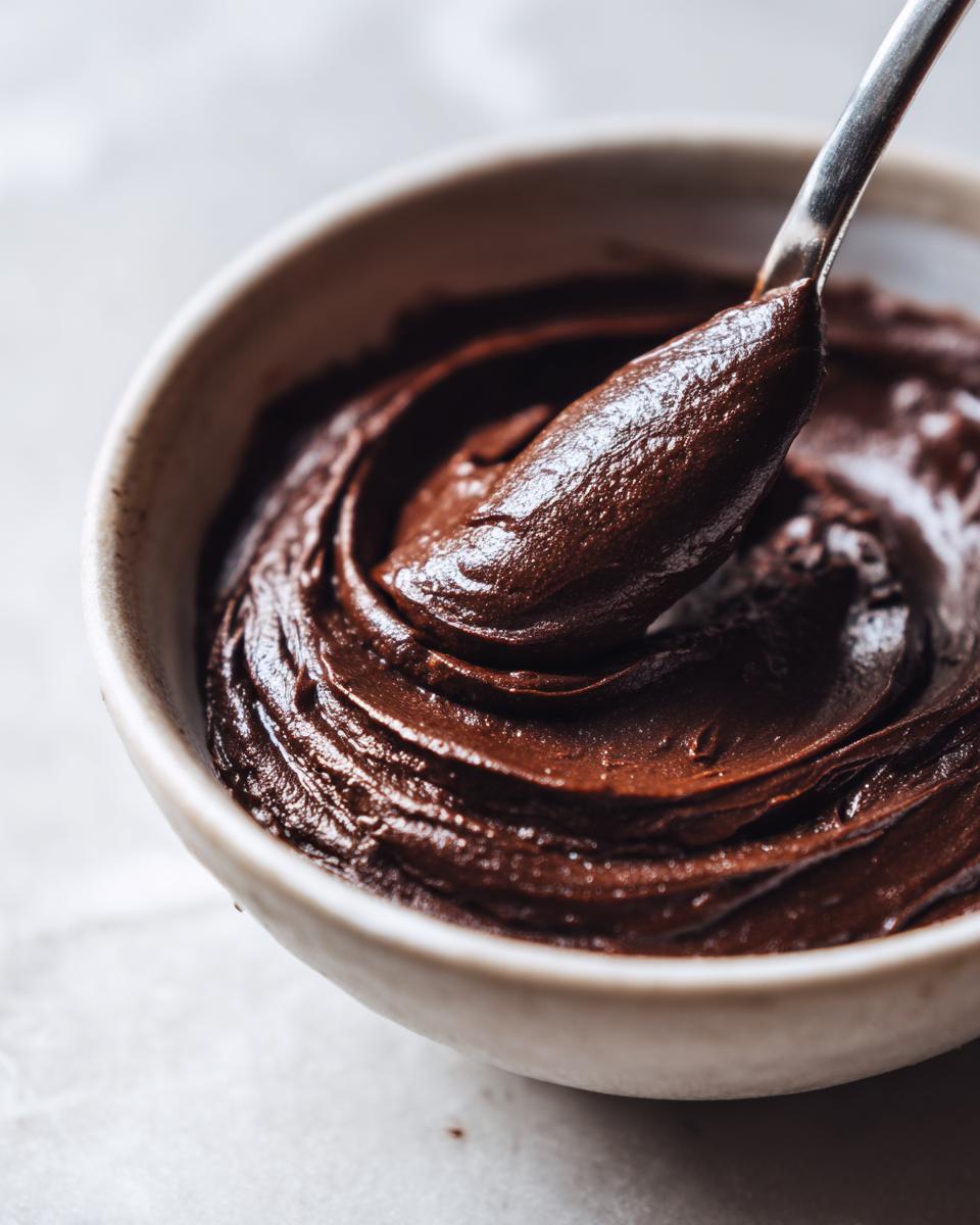 Close-up of rich, dark chocolate pudding being scooped from a bowl with a silver spoon.