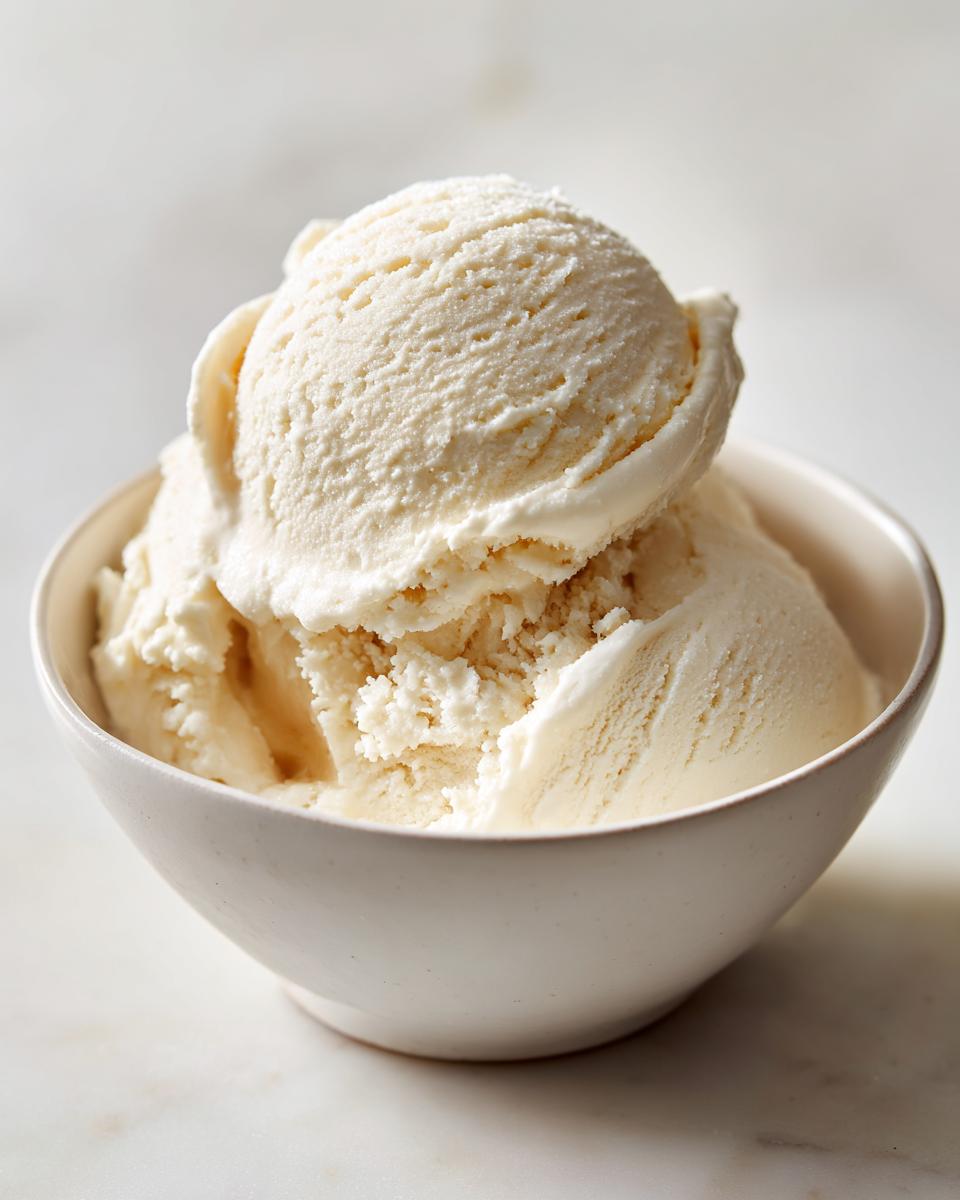 Close-up of two scoops of creamy, pale vanilla cottage cheese ice cream served in a small white bowl.