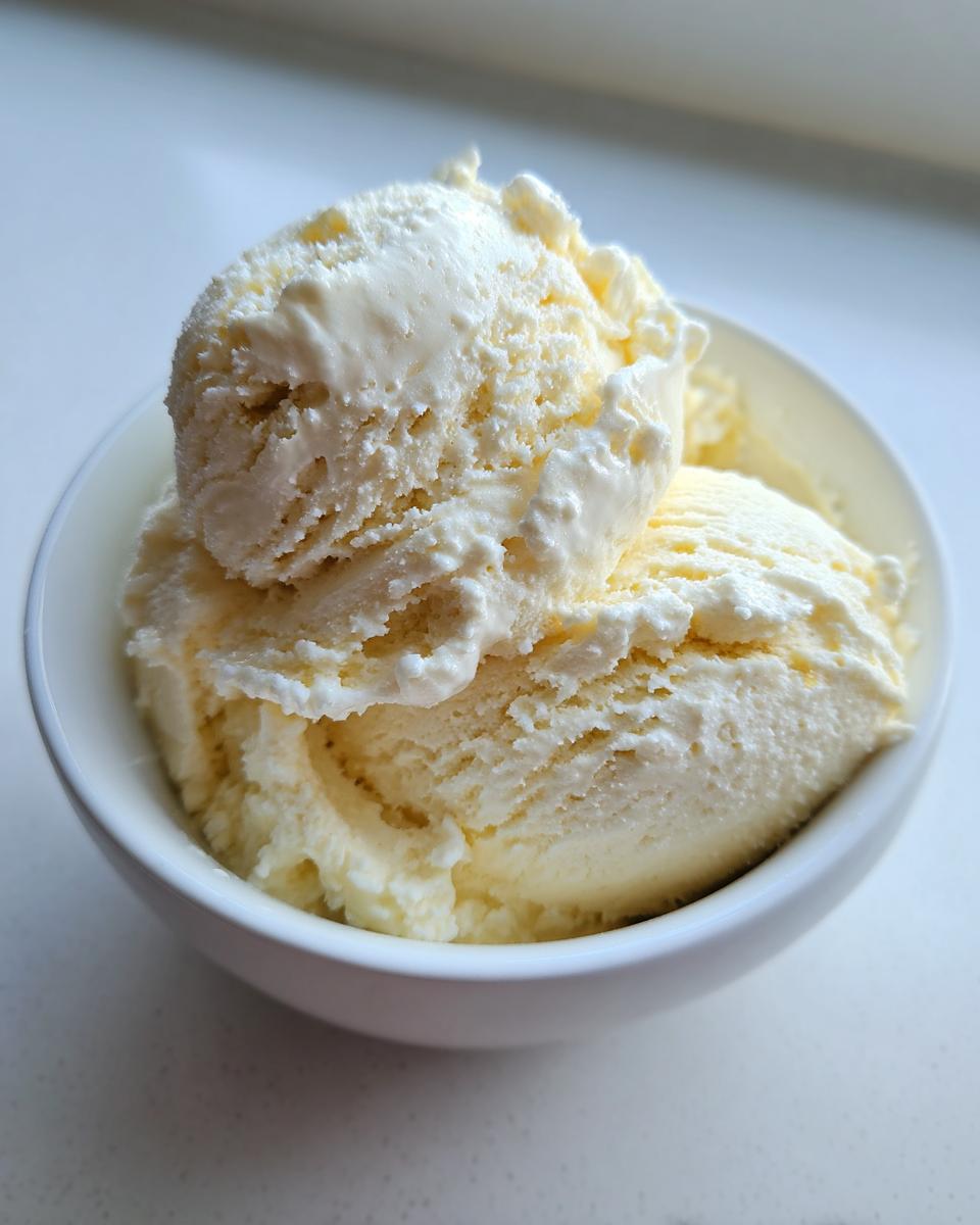 Two generous scoops of creamy, pale yellow cottage cheese ice cream served in a small white bowl.