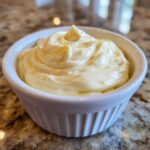 Close-up of creamy, pale yellow homemade mayonnaise swirled beautifully in a small white ramekin.