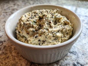 Close-up of a creamy, textured olive dip speckled with dark olive pieces, served in a white ribbed bowl.