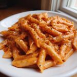 A close-up of penne pasta generously coated in creamy pink sauce pasta and sprinkled with black pepper.