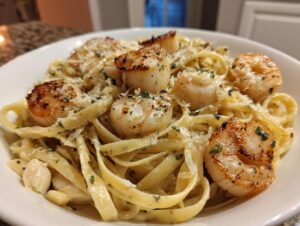 Close-up of creamy seafood pasta featuring perfectly seared scallops and shrimp, topped with Parmesan cheese.