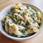 Close-up of creamy pasta mixed with spinach and artichoke pieces, representing a spinach artichoke meal.
