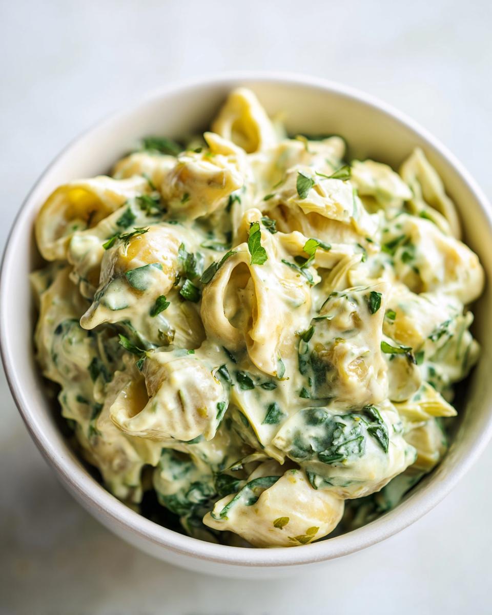 Close-up of creamy pasta coated in a rich spinach artichoke sauce, garnished with fresh parsley.