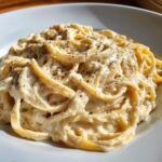 Close-up of fettuccine pasta generously coated in creamy vegan alfredo sauce and topped with cracked black pepper.
