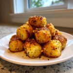 A pile of golden brown, crispy air fryer gnocchi seasoned with herbs and Parmesan cheese on a white plate.