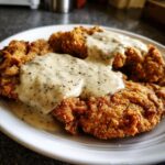Two pieces of golden, crispy chicken fried steak smothered in thick, black pepper-flecked country gravy.