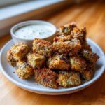 A plate piled high with golden brown, crispy Fried Pickles next to a small bowl of creamy green dipping sauce.