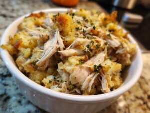 Close-up of shredded chicken mixed with stuffing in a white bowl, representing crock pot chicken and stuffing.