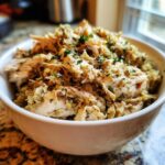 Close-up of moist, shredded crock pot chicken and stuffing mixture topped with herbs in a white bowl.