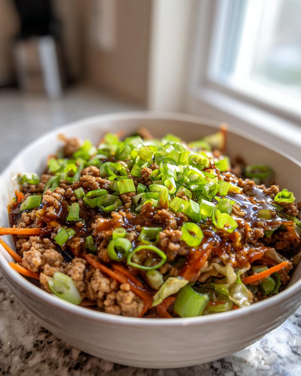 A close-up of a white bowl filled with savory Egg Roll in a Bowl, topped generously with fresh green onions.