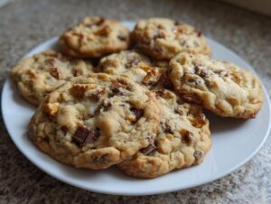 A white plate piled high with freshly baked, chewy kitchen sink cookies loaded with chocolate chunks and other mix-ins.