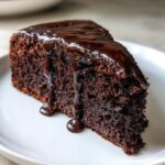A decadent slice of flourless chocolate cake topped with thick, glossy chocolate ganache dripping down the sides.