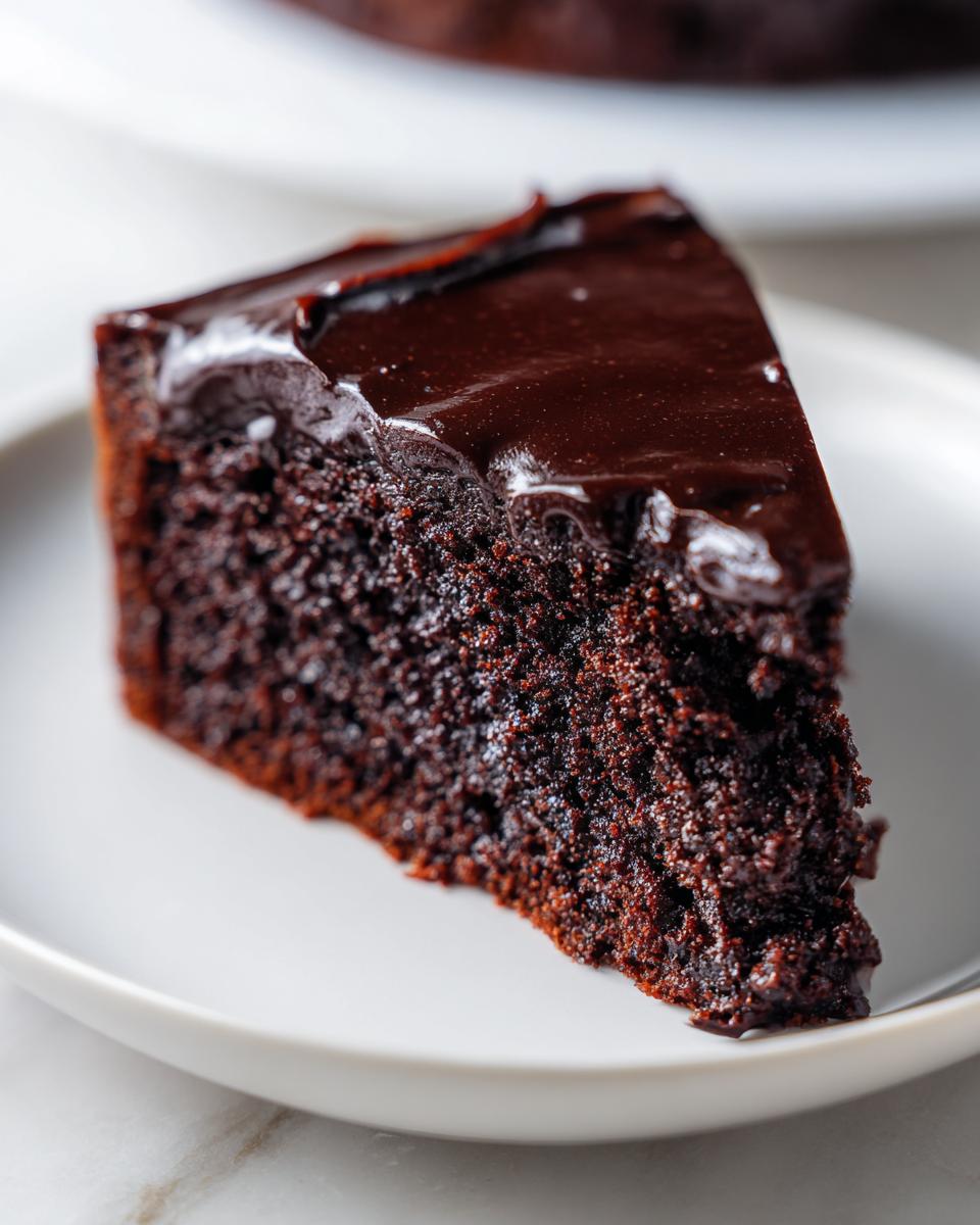 Close-up of a moist slice of flourless chocolate cake topped with glossy dark chocolate ganache.