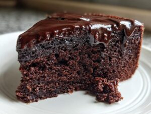Close-up of a moist slice of flourless chocolate cake topped with glossy, dripping chocolate ganache.