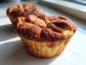 A close-up of a freshly baked french toast muffin topped with a thick layer of cinnamon sugar.