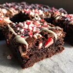 Close-up of a fudgy candy cane brownie topped with white chocolate drizzle and crushed peppermint pieces.