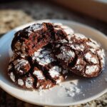 Close-up of fudgy chocolate crinkle cookies dusted with powdered sugar on a white plate.