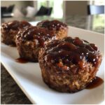 Close-up of three glazed mini meatloaf muffins served on a white rectangular plate.