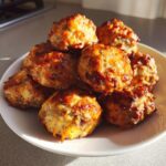 A pile of freshly baked, golden brown bisquick sausage balls stacked on a white plate.