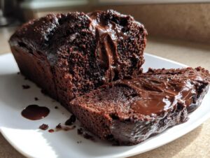 A slice of rich, dark chocolate hot fudge brownie bread oozing with melted chocolate fudge on a white plate.
