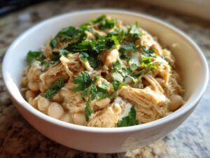 A close-up of a white bowl filled with instant pot white chicken chili, topped with fresh cilantro.