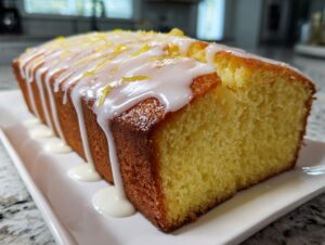 A close-up of a freshly baked lemon pound cake, drizzled with white glaze and lemon zest.