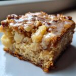 Close-up of a moist, square apple brownies slice topped with nuts and a thin vanilla glaze.