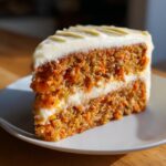 Close-up of a moist slice of carrot cake recipe with visible shredded carrots and thick cream cheese frosting.