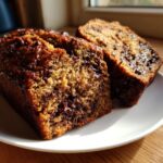 Two slices of incredibly moist chocolate banana bread showing melted chocolate chips on a white plate.