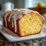 Close-up of a moist slice of lemon pound cake topped with thick white glaze and lemon zest.