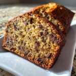 Close-up of two moist slices of vegan banana bread loaded with chocolate chips on a white plate.