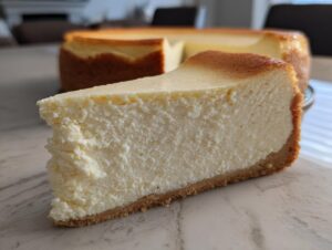 A thick, creamy slice of Protein Cheesecake with a golden brown top and graham cracker crust.