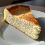 A thick, fluffy slice of baked Protein Cheesecake with a golden-brown top, served on a white plate.
