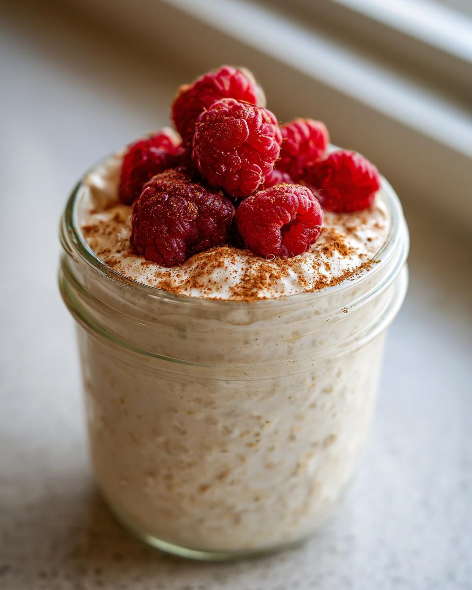 Close-up of creamy overnight oats topped with fresh raspberries and a dusting of cinnamon.
