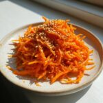 Close-up of a bright orange raw carrot salad, shredded and topped generously with toasted sesame seeds.