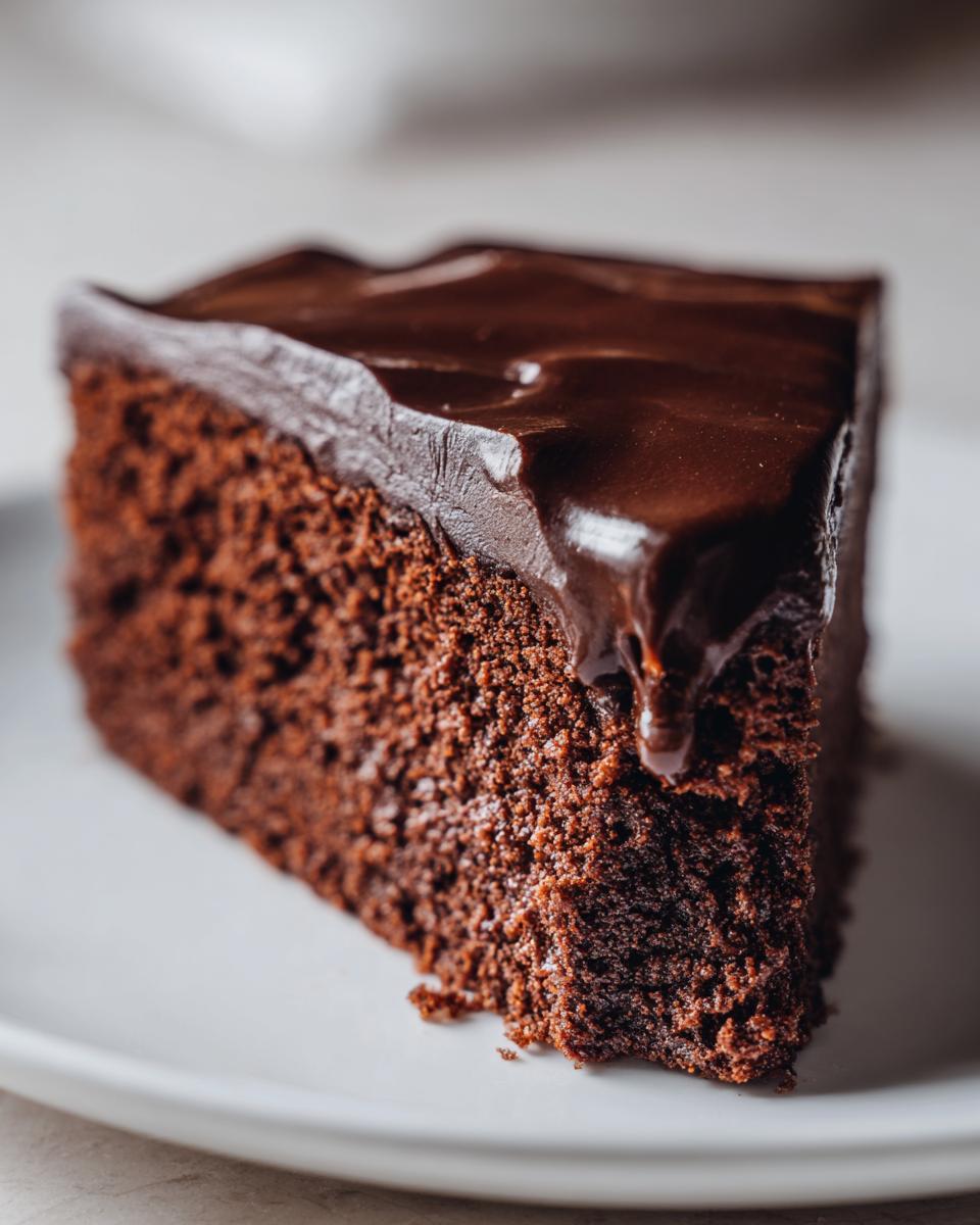 Close-up of a moist slice of flourless chocolate cake topped with dripping dark chocolate ganache.
