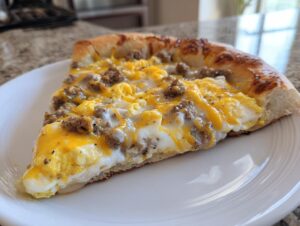 A thick slice of sausage gravy breakfast pizza topped with scrambled eggs, sausage crumbles, and melted cheddar cheese.