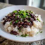 Close-up of a white bowl filled with fluffy white rice topped generously with seasoned black beans and fresh chopped cilantro, a perfect beans and rice dish.