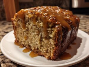 Close-up of a moist slice of apple dapple cake topped with thick, dripping caramel sauce.