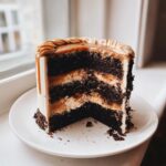 A tall slice of dark chocolate capricorn cake with multiple layers of filling and a rich caramel drip topping.