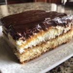 Close-up of a square slice of eclair cake showing layers of pastry, cream, and chocolate frosting.