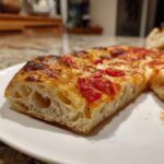 A close-up cross-section of a slice of pizza made with sourdough discard pizza dough, showing a light, airy, open crumb structure.