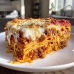 A thick, layered slice of spaghetti pie with meat sauce and melted mozzarella cheese on top.