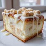 A rich, thick slice of sugar cookie cheesecake topped with white glaze and cookie pieces.